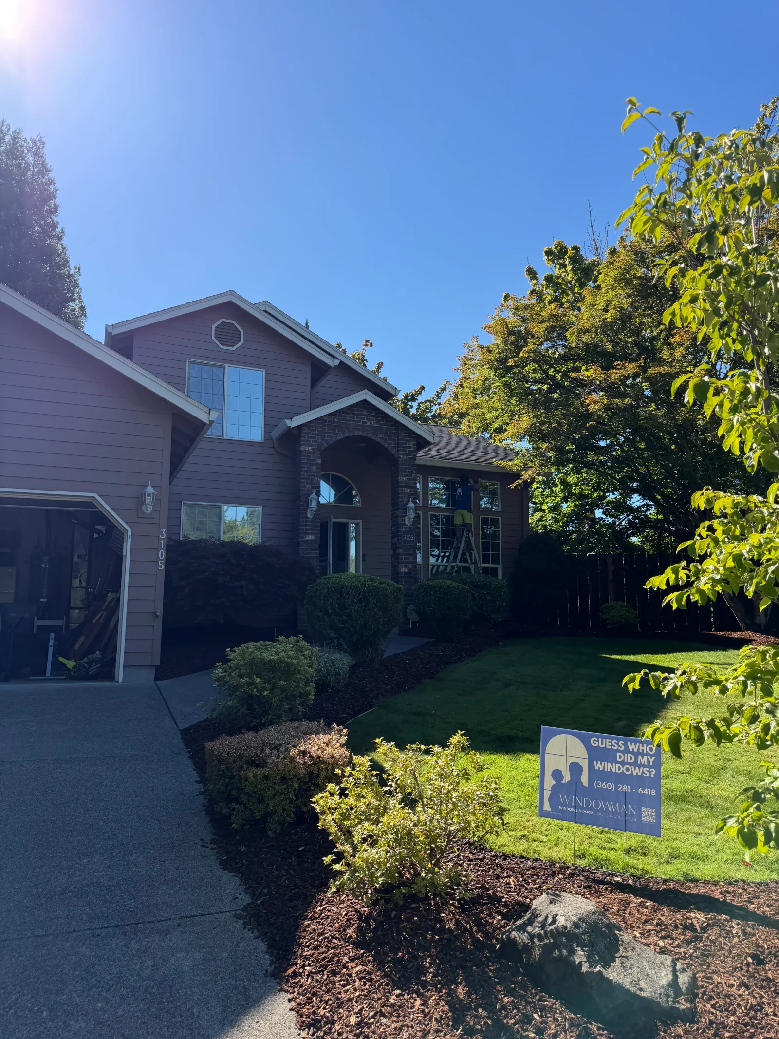 Two-story home with mauve lap siding, brick entry arch, and grid-pane windows; Windowman yard sign in lawn