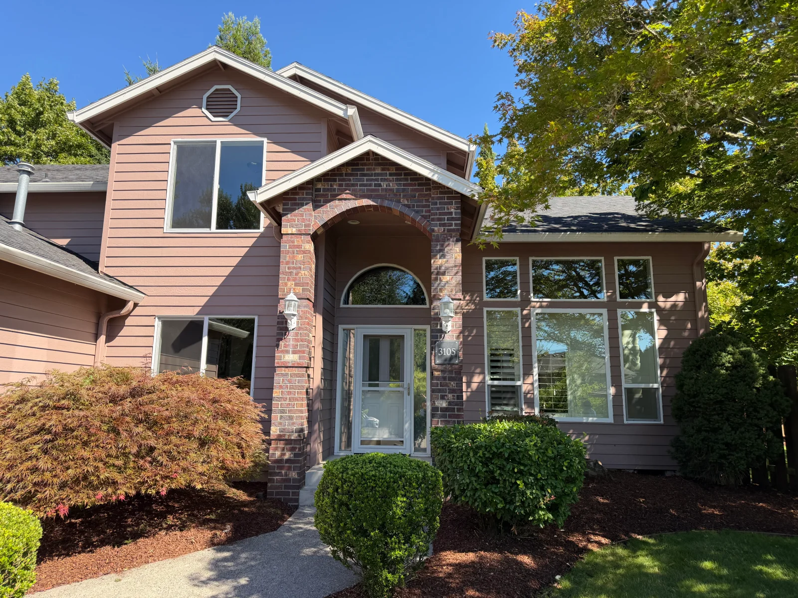Two-story home with mauve lap siding, brick arched entry, and white-framed windows including a large picture window