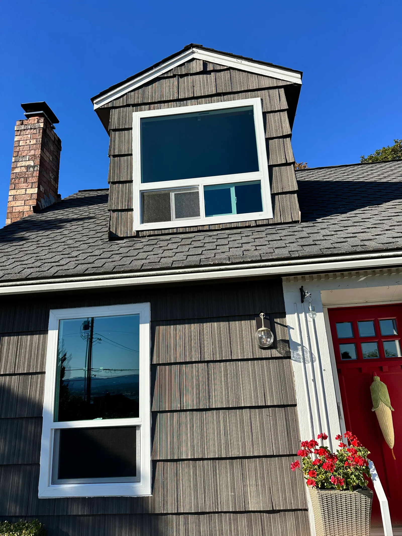 White vinyl windows installed in a gabled dormer and tall double-hung unit on wood shingle siding with asphalt roof
