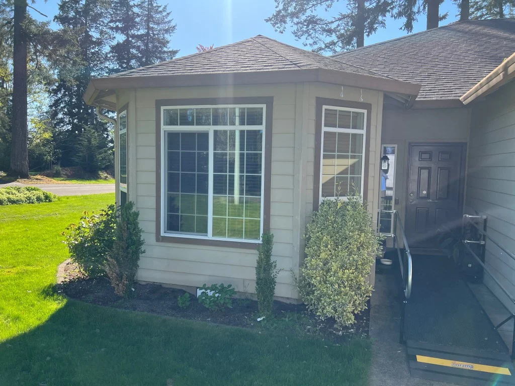 Cream lap-siding home with brown-trimmed bay window and white grid-pane vinyl windows beside a brown entry door